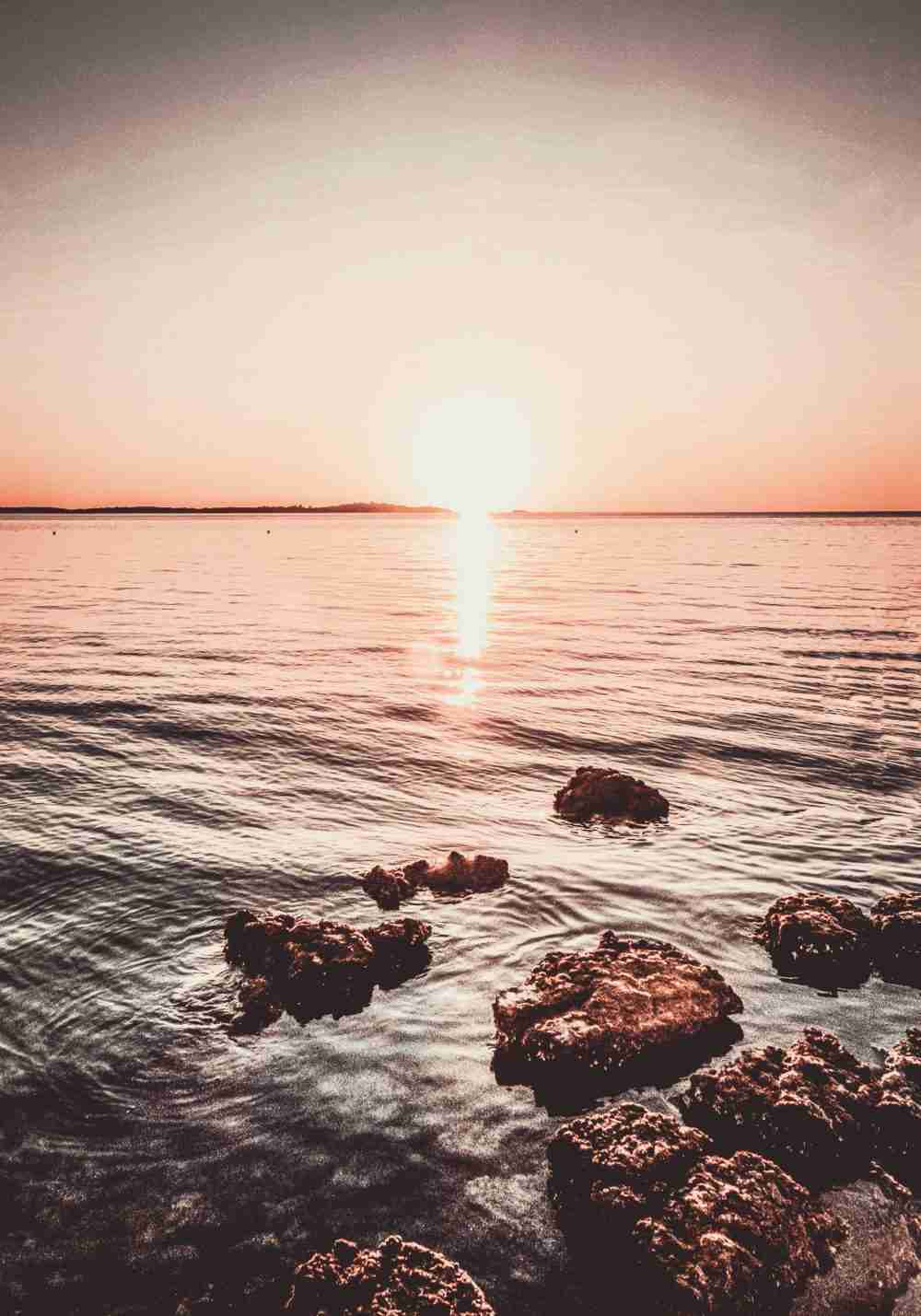 Vacker Solnedgång på en stenig Stranden Poster